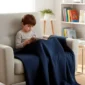 Child reading in a chair while using a navy weighted blanket.