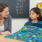 Child using a navy weighted blanket in a classroom with adult support.