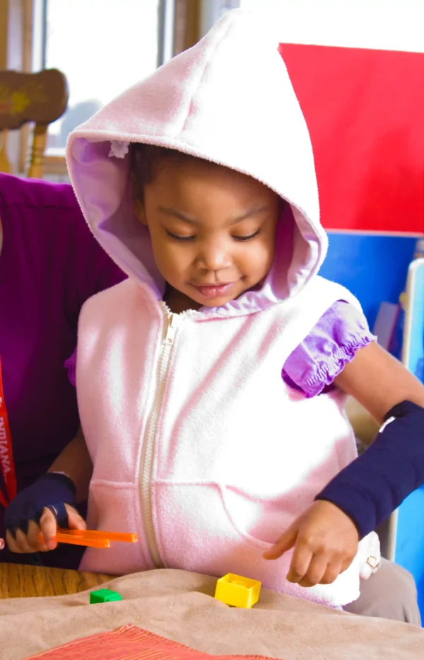 Pink Hooded Weighted Sensory Vest for Children Child wearing a pink hooded weighted sensory vest while playing with blocks.